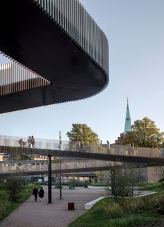 two people walking on a walkway under a bridge