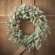 a christmas wreath hanging on a wooden door with red berries and pine cones around it