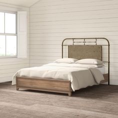 a bed sitting in a bedroom next to a window with white walls and wood flooring