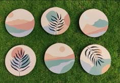 four coasters with palm leaves painted on them sitting in the middle of some grass