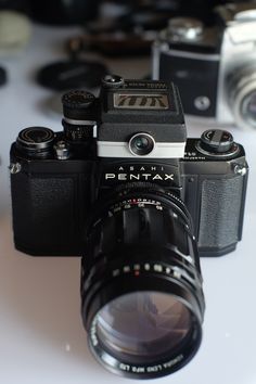 an old camera sitting on top of a white table next to other cameras and lenses