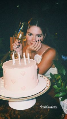 a woman sitting in front of a cake with candles on it and holding a wine bottle