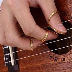 a person with two gold rings on their fingers playing an ukulele guitar string