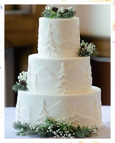 a three tiered white wedding cake decorated with greenery and pine cones on top