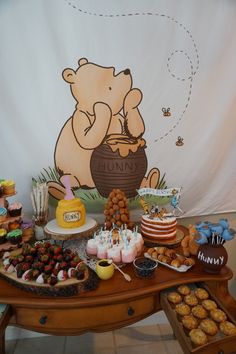 a wooden table topped with lots of desserts next to a giant teddy bear banner