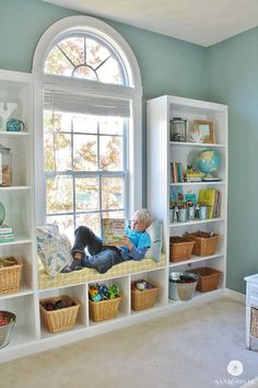 a child sitting on a window sill in front of a book shelf filled with books