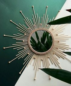 a round mirror with sticks sticking out of it's center surrounded by green leaves