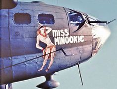 a woman is sitting on the nose of an old style airplane with miss hinookie painted on it