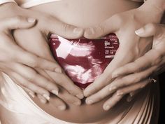 a pregnant woman's stomach with her hands in the shape of a red heart