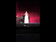 a woman standing on top of a stage next to a piano