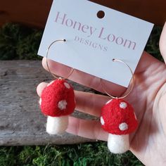 a pair of red and white mushroom earrings with gold hoops are shown in front of a sign that says honey loom designs