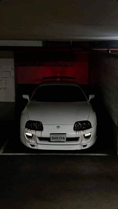 a white car parked in a parking garage next to a red light on the wall