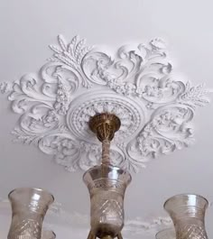 an ornately decorated ceiling in a white room with glass vases on the floor