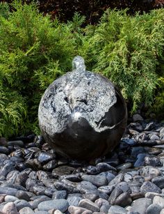 a large black ball sitting on top of a pile of rocks next to trees and bushes