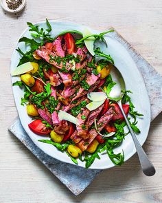 a white plate topped with meat and veggies on top of a wooden table