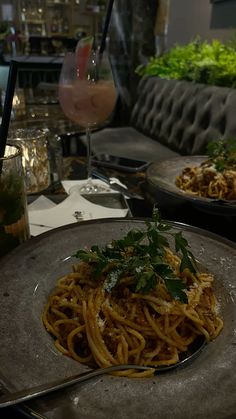 a plate of spaghetti with parsley on top and a glass of wine in the background