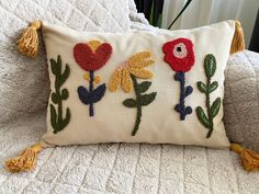 a decorative pillow with flowers and tassels on it sitting on a white bed