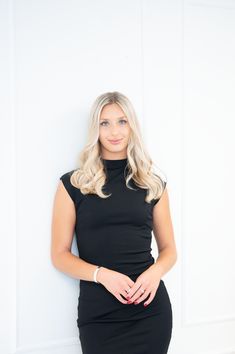 a beautiful blonde woman in a black dress posing for the camera with her hands on her hips