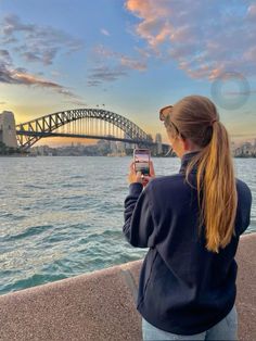 a woman taking a photo of the sydney harbour bridge