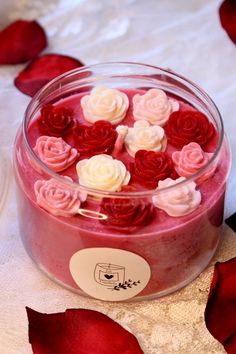 red and white flowers in a glass container on a table with rose petals around it