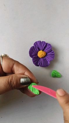 a hand holding a pink toothbrush next to a purple flower with green leaves on it