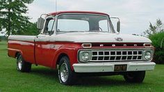 an old red and white truck is parked in the grass