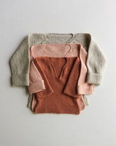 three sweaters sitting next to each other on top of a white surface, one in pink and the other in grey