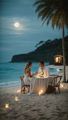 a man and woman sitting at a table on the beach with candles in front of them