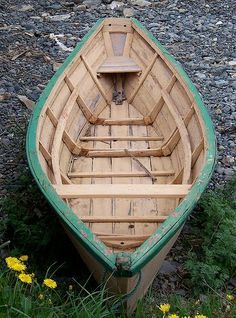 a small wooden boat sitting on top of a grass covered field next to yellow flowers