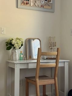 a white desk with a mirror, chair and vase on it in a small room