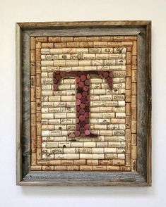 the letter t made out of wine corks is mounted on a wall with a wooden frame