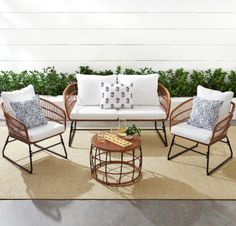 an outdoor patio with wicker furniture and pillows on the floor, next to a potted plant