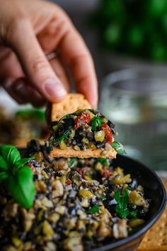 a person is dipping some food into a black dish with spinach and other vegetables