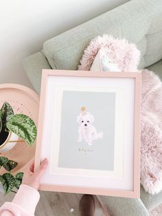 a person holding up a pink framed print with a white poodle on it