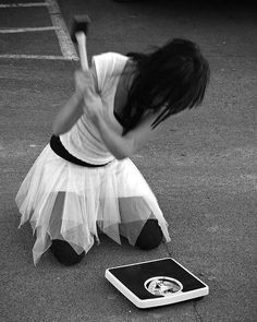 a woman holding a baseball bat standing next to a laptop computer on the ground in a parking lot