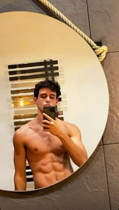 a shirtless man taking a selfie in front of a mirror with his cell phone