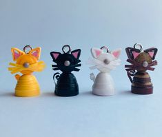 four different colored cat keychains on a white surface with one black, one yellow and one red