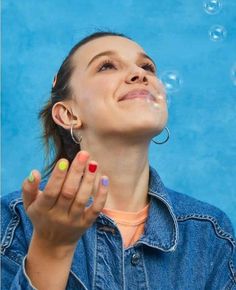 a woman blowing bubbles in the air with her eyes closed and one hand on her face