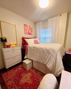 a white bed sitting next to a window on top of a red rug in a bedroom