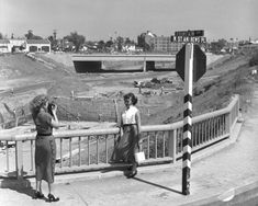 black and white photograph of two women standing on a bridge with construction in the background