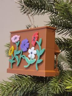 an ornament hanging from a christmas tree decorated with colorful flowers and green leaves