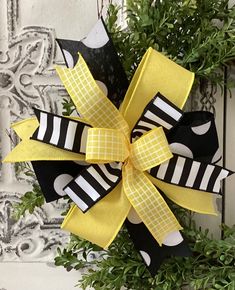 a yellow and black bow hanging from the side of a door with greenery around it