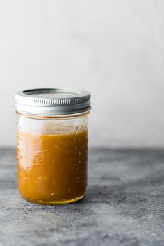 a glass jar filled with orange sauce on top of a counter next to a white wall