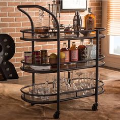 a bar cart with wine glasses and liquor bottles on the bottom shelf in front of a brick wall