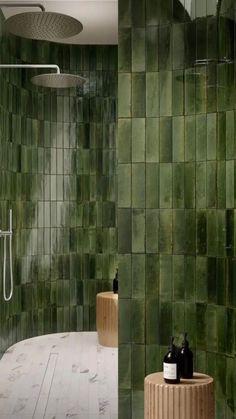 a bathroom with green tiles on the walls and floor, along with two wooden stools