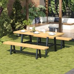 an outdoor dining area with benches and tables in the grass, surrounded by greenery