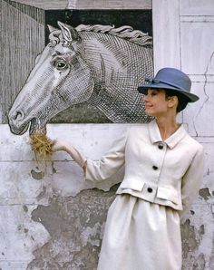 a woman in a white coat and hat standing next to a horse head on a wall