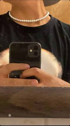 a person holding a cell phone in front of a wooden table with a white beaded necklace on it