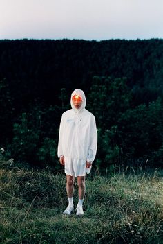 a person wearing a white outfit standing on top of a grass covered field with trees in the background