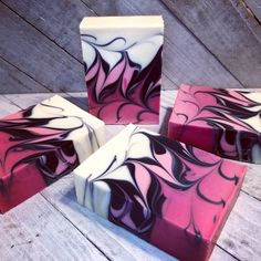 four soap bars sitting on top of each other in front of a wooden table with white and pink swirls